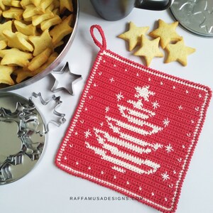 K&ouml;nnte beinhalten: Ein roter geh&auml;kelter Topflappen mit einem wei&szlig;en geh&auml;kelten Weihnachtsbaum-Design. Der Topflappen hat eine Schlaufe zum Aufh&auml;ngen. Der Text "RAFFAMUSADESIGNS.COM" befindet sich am unteren Rand des Topflappens.