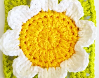 May include: A crocheted flower square with a yellow center and white petals. The square is surrounded by a green border.