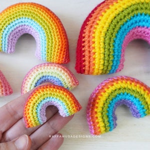 Op de afbeelding: Een set van vijf gehaakte regenboogbogen in verschillende maten. De bogen zijn gemaakt van kleurrijk garen in tinten rood, oranje, geel, groen, blauw en paars. De bogen zijn gerangschikt op een wit houten oppervlak.