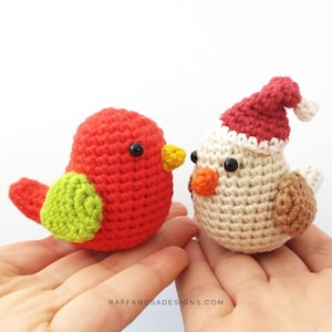 Puede incluir: Dos adornos de pájaros de crochet, uno rojo con alas verdes y un pico amarillo, el otro blanco con alas marrones y un gorro de Papá Noel rojo.