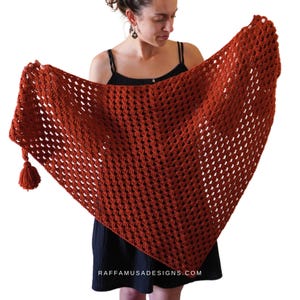 May include: A rust-colored crochet shawl with a fringe tassel. The shawl is made with a lacy stitch pattern and is draped over a person's shoulders.