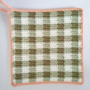 May include: A crocheted pot holder with a green and white gingham pattern and a peach colored border.