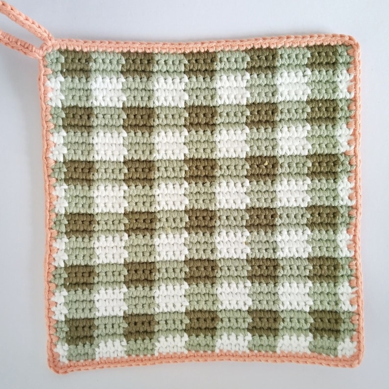 May include: A crocheted pot holder with a green and white gingham pattern and a peach colored border.