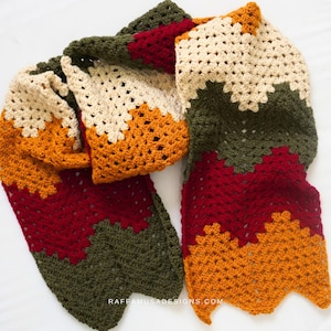 Puede incluir: Bufanda de ganchillo hecha a mano con un patrón de chevrón. La bufanda presenta bandas de colores alternas que incluyen verde oliva, burdeos, beige y naranja. La bufanda está hecha de hilo suave y es adecuada para el otoño o el invierno.