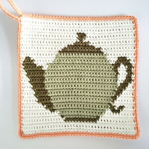May include: A crocheted pot holder with a teapot design. The teapot is green and the pot holder is white with a peach border.