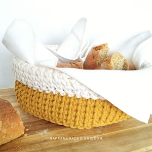 May include: A crocheted bread basket with a white top and a mustard yellow bottom. The basket is filled with bread and a white cloth napkin.