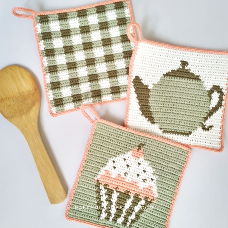 May include: Three crocheted pot holders with a peach border. One pot holder has a brown and white checkered pattern. Another pot holder has a green teapot design. The third pot holder has a green cupcake design with a pink frosting and white sprinkles.