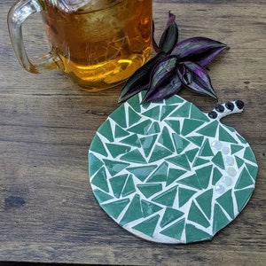 May include: A green mosaic apple-shaped coaster with white and black accents. The coaster is made of small triangular tiles and has a glossy finish.