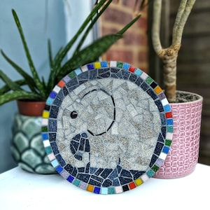 May include: A grey mosaic tile elephant design with a colourful border. The tile is round and has a glossy finish.