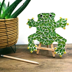 May include: A green mosaic frog figurine on a wooden easel. The frog is made of small green and yellow glass tiles.