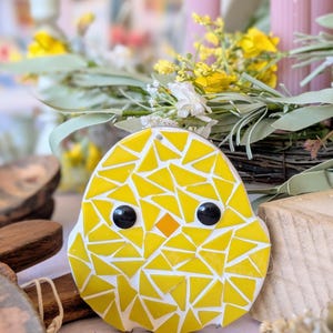 May include: A yellow mosaic chick ornament with black eyes and an orange beak. The chick is made of yellow triangular tiles with white grout. Suitable for Easter or spring decorations.