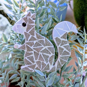 May include: A gray and white mosaic squirrel figurine with a white tail. The squirrel is made of small, triangular pieces of glass or tile.