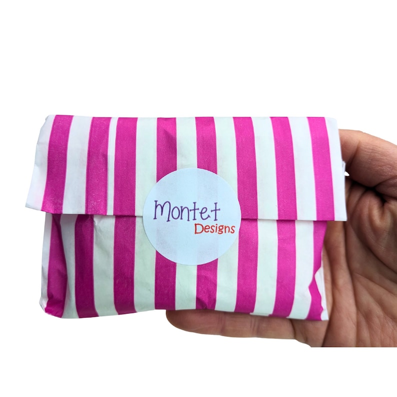 May include: A pink and white striped paper bag with a white circle sticker that says "Montet Designs" in purple and red lettering.