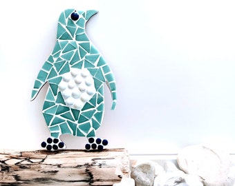 May include: A teal blue mosaic penguin figurine with white and black details. The penguin is standing on a piece of driftwood.