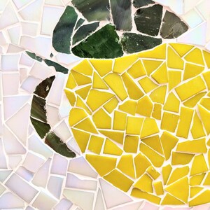 May include: A mosaic artwork depicting a lemon with a green leaf. The lemon is made of small yellow tiles, and the leaf is made of small green tiles. The background is made of small white tiles.