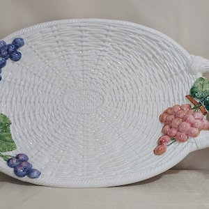 May include: White oval ceramic serving tray with a woven basket design. The tray has two handles with grapes and leaves sculpted on each side.