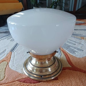May include: A white glass ceiling light fixture with a brass base. The fixture has a rounded, dome-shaped glass shade.