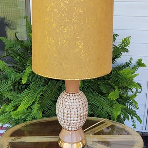 May include: A mid-century modern table lamp with a brown ceramic base and a textured white design. The lamp has a gold-colored trim and a beige lampshade with a gold flecked pattern.