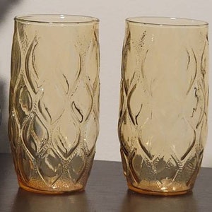 May include: Two amber glass drinking glasses with a diamond pattern. The glasses are empty and sitting on a brown surface.
