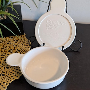 May include: A handmade wooden sign with the text "Welcome to our home" in a handwritten style. The sign is painted white with a distressed finish and a black border. A small, decorative heart is attached to the bottom.