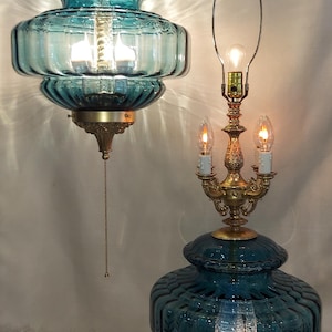 May include: A teal glass pendant light and table lamp with brass accents. The pendant light hangs from a chain and has a pull chain. The table lamp has a three-light candelabra base. Both have a ribbed design.