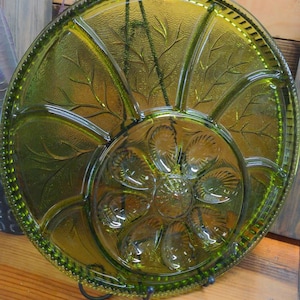 May include: A green glass serving dish with a scalloped edge and a floral design in the center. The dish has seven sections for serving different foods.