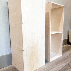 May include: Two unfinished wooden shelves, one tall and narrow, the other shorter and wider, both made of plywood.