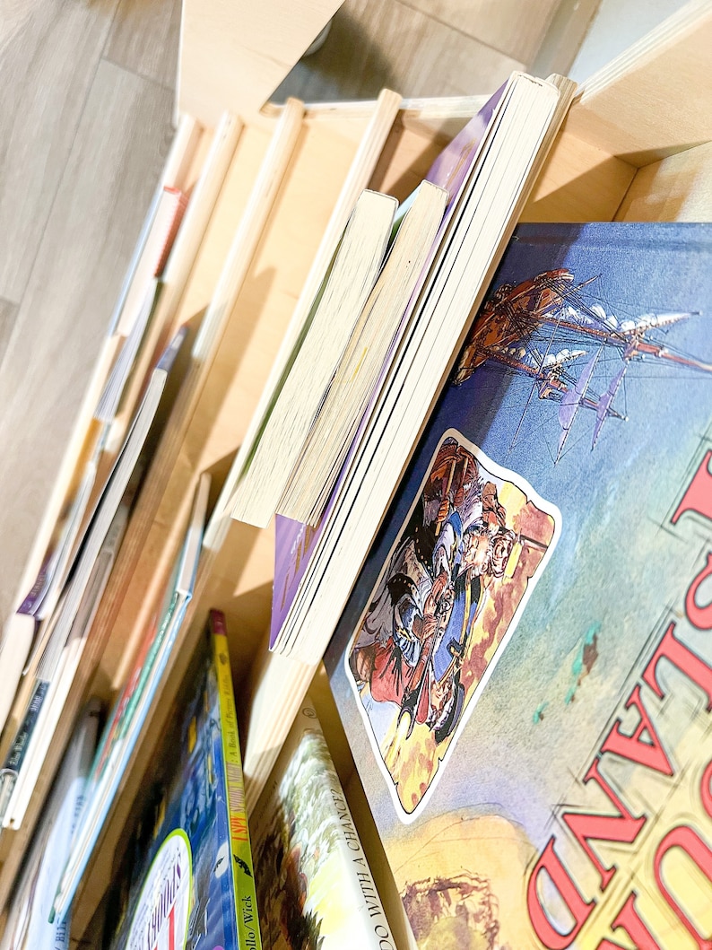 May include: A wooden bookshelf filled with various books. The books have colorful covers and different sizes. Some books are standing upright, while others are lying down. The bookshelf is made of light-colored wood.