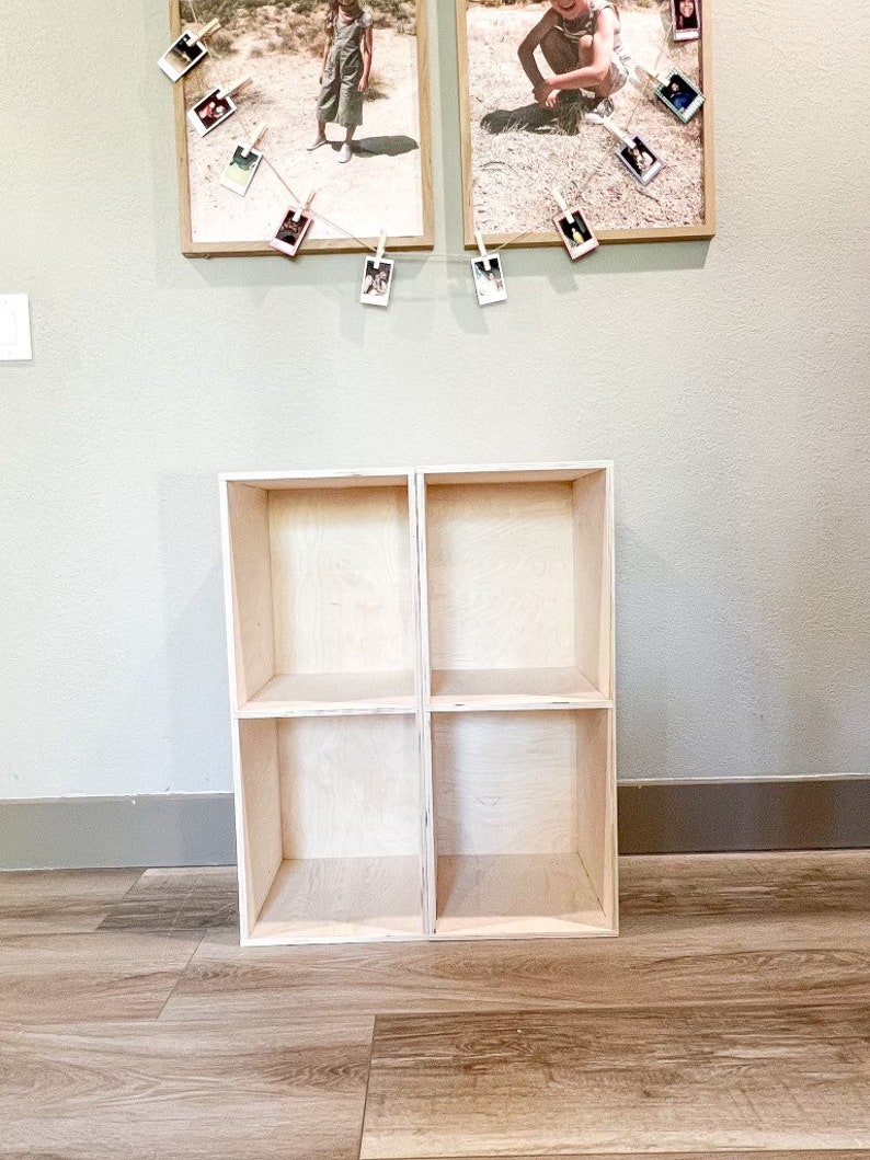 May include: A light wood shelf unit with four open cubbies. The shelf unit is standing on a light wood floor.