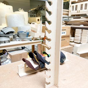May include: A wooden hat rack with 10 slots for storing baseball caps. The rack is made of light-colored wood and has a simple design. There are several baseball caps hanging on the rack.
