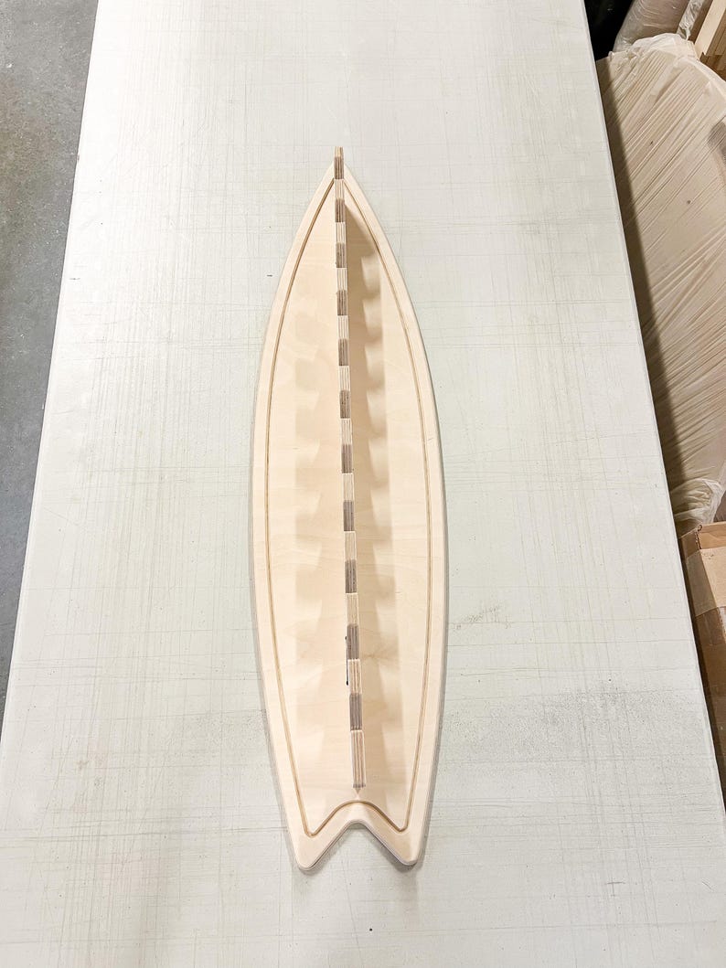 May include: A wooden surfboard rack with slots for storing multiple surfboards. The rack is made of light-colored wood and has a surfboard shape.