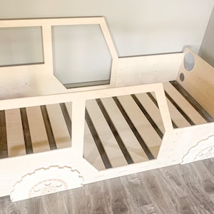 May include: A wooden bed frame shaped like a truck, with a slatted base and cut-out details for windows and tyres.