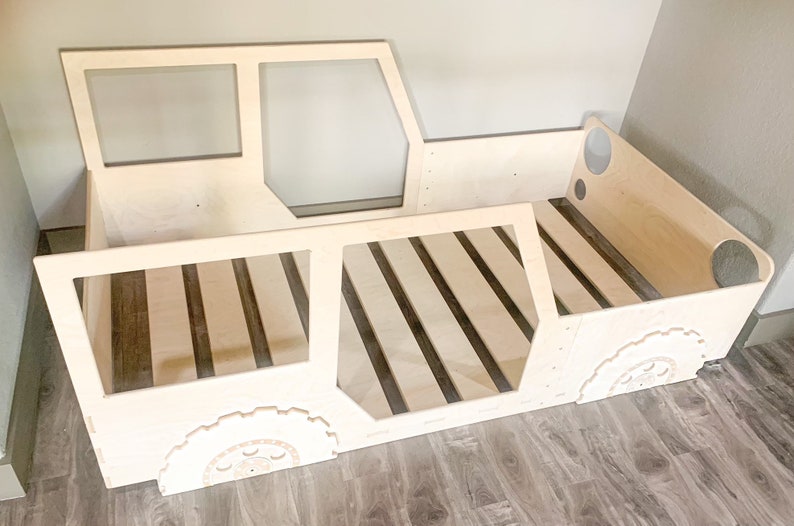 May include: A wooden bed frame shaped like a truck, with a slatted base and cut-out details for windows and tyres.
