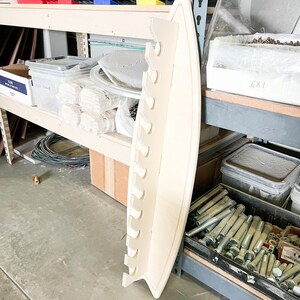 May include: A white wooden shelf unit with multiple slots for storage. The shelf is curved and has a rounded edge. The shelf is empty and ready to be used.