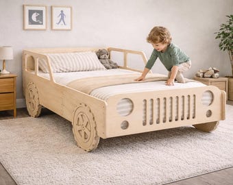 May include: A light-colored wooden bed frame designed to resemble a jeep. The bed has large, circular wheels and a front grill. The bed is made of light-colored wood and has a mattress with a striped pillow and a beige blanket. A child is playing on the bed.