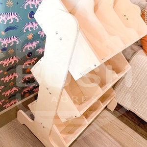 May include: A wooden toy shelf with multiple compartments and shelves. The shelf is made of natural wood and has a light brown colour. The shelf is designed to be used by children and has a playful, whimsical design.