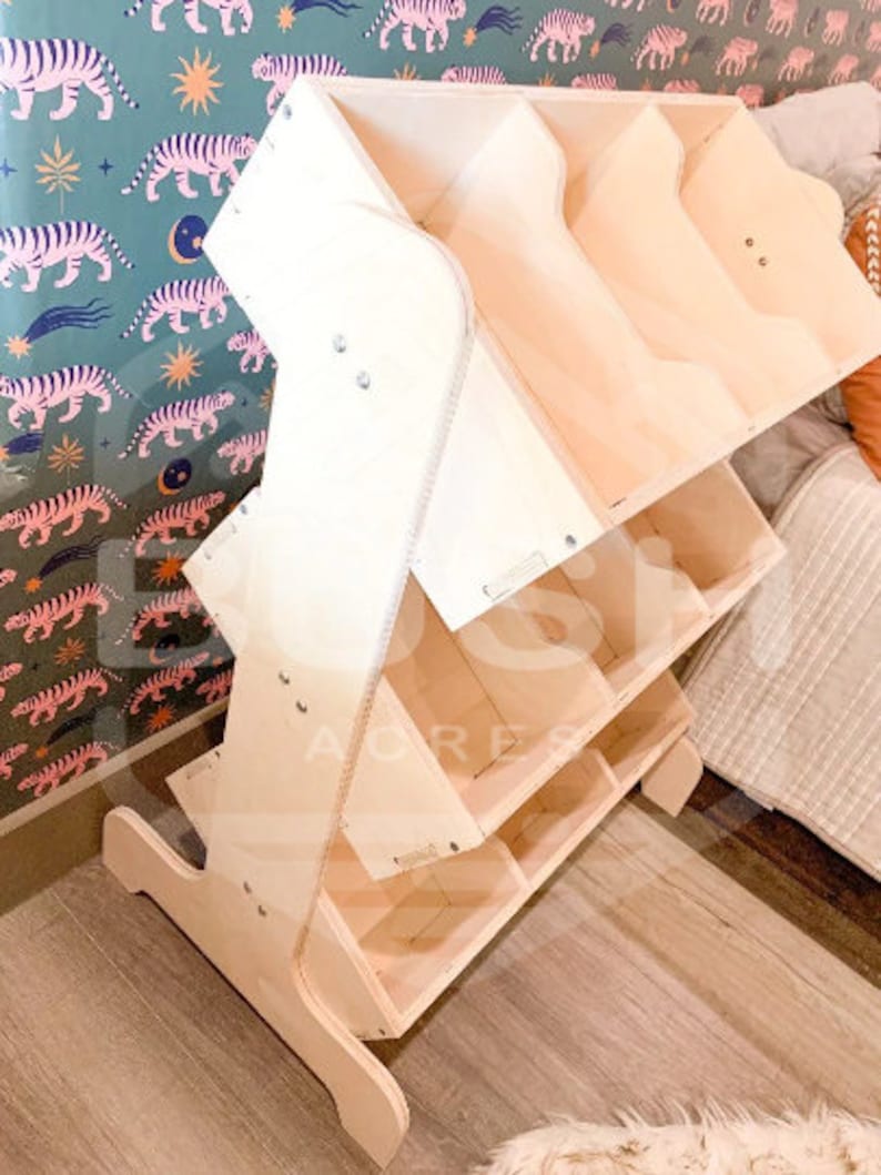 May include: A wooden toy shelf with multiple compartments and shelves. The shelf is made of natural wood and has a light brown colour. The shelf is designed to be used by children and has a playful, whimsical design.