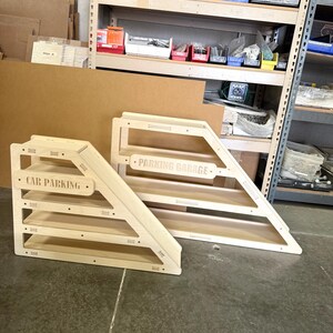 May include: Two wooden car parking garages. One is labeled "CAR PARKING" and the other is labeled "PARKING GARAGE". Both have a natural wood finish and a triangular design with multiple shelves for toy cars.