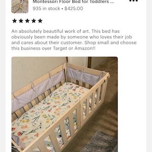 May include: A light wood Montessori floor bed for toddlers with a white and floral patterned sheet. The bed has a removable side rail and a gray padded headboard.