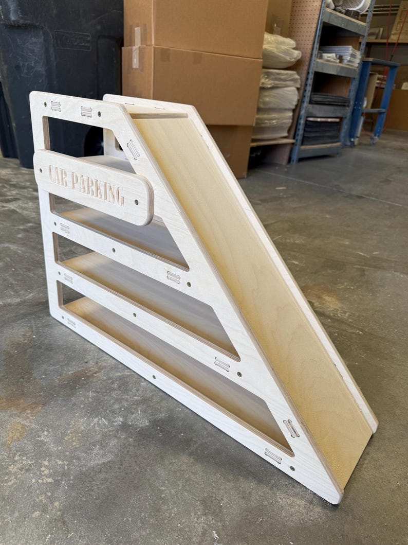 May include: A wooden car parking ramp with a natural wood slide and white frame. The words "CAR PARKING" are engraved on the top. The ramp has three parking levels and is designed for toy cars.