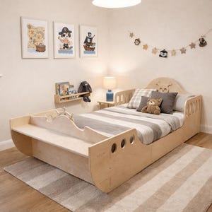 Può includere: Un letto in legno chiaro a tema pirata, con una testiera con un design a forma di cervo e una pediera abbinata. Il letto è completato da una trapunta a righe, cuscini e un orsacchiotto. Tre quadri a tema pirata incorniciati sono appesi alla parete.