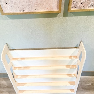 May include: A white wooden bookshelf with a unique design. The bookshelf has multiple shelves and a sturdy base. The sides of the bookshelf are curved, adding a touch of elegance. The bookshelf is perfect for storing books, toys, or other items.