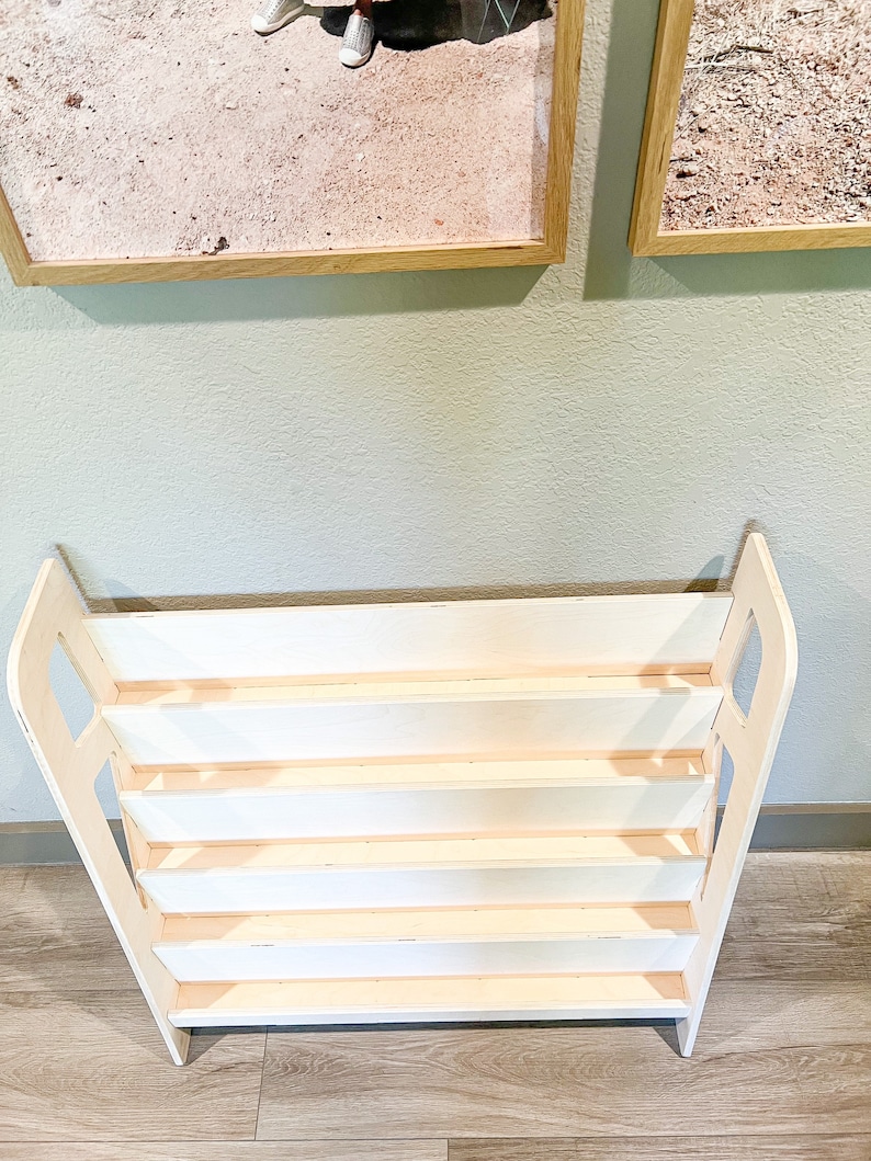May include: A white wooden bookshelf with a unique design. The bookshelf has multiple shelves and a sturdy base. The sides of the bookshelf are curved, adding a touch of elegance. The bookshelf is perfect for storing books, toys, or other items.