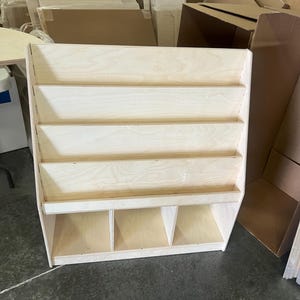May include: A wooden bookshelf with five shelves and four storage compartments at the bottom. The bookshelf is made of light-colored wood and has a natural finish.
