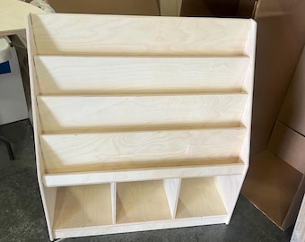May include: A wooden bookshelf with five shelves and four storage compartments at the bottom. The bookshelf is made of light-colored wood and has a natural finish.