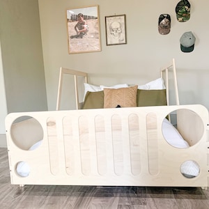 May include: A wooden bed frame shaped like a jeep, with a white mattress and pillows. The bed is in a room with a light brown wood floor and white walls.