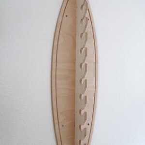 May include: A wooden surfboard-shaped wall rack with multiple cut-out hooks for hanging items. The rack is made of light-colored wood and has a natural finish.