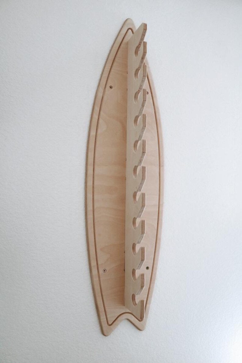May include: A wooden surfboard-shaped wall rack with multiple cut-out hooks for hanging items. The rack is made of light-colored wood and has a natural finish.