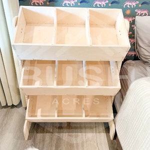 May include: A wooden toy storage shelf with four shelves. The top shelf has three compartments. The bottom three shelves have four compartments each. The shelf is made of natural wood and has a light brown finish.