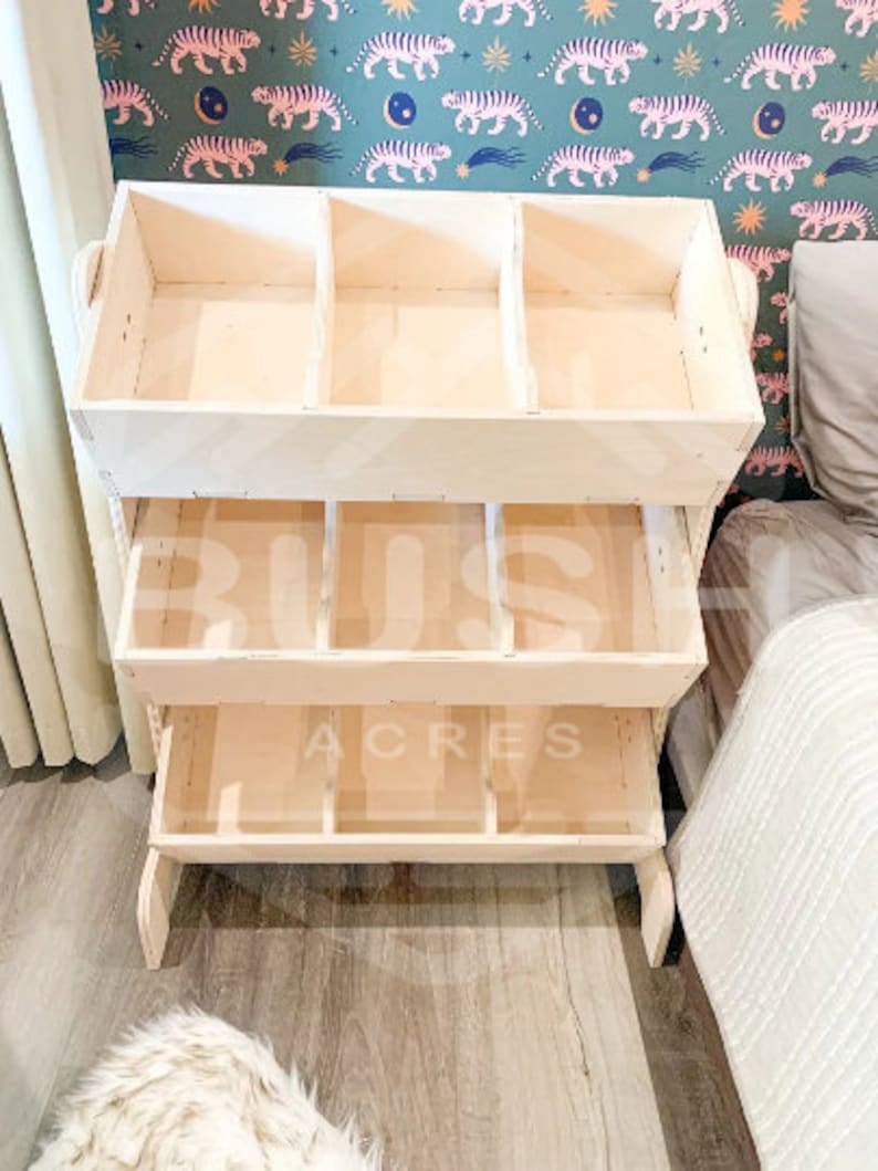 May include: A wooden toy storage shelf with four shelves. The top shelf has three compartments. The bottom three shelves have four compartments each. The shelf is made of natural wood and has a light brown finish.